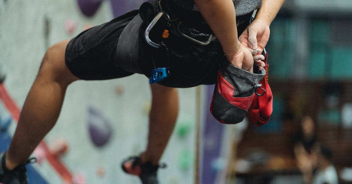 How to protect my gear during a monsoon? - Unrecognizable crop male climber in safety equipment hanging near climbing wall while putting hands in bag with talcum powder in bouldering hall