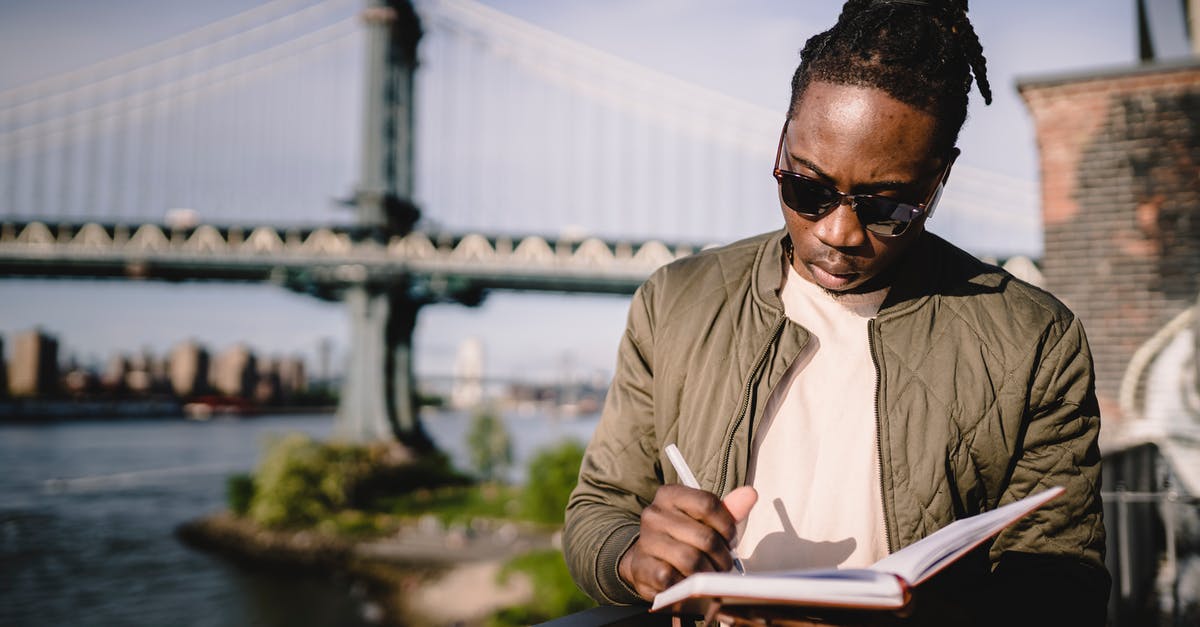 How to read Donan bus schedule (Hokkaido) - Concentrated young black male checking schedule in notebook while standing on city promenade against bridge on sunny day