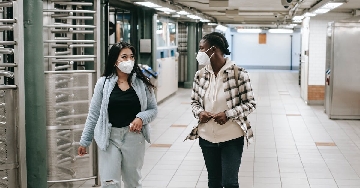 How to safely transport money? - Multiracial women in protective masks walking together in hallway of subway and looking at each other