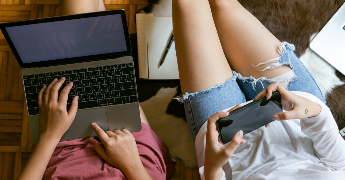 How to search for weekend flights? - From above of crop girlfriends in home clothes sitting on floor with laptop and smartphone while spending time together and planning weekend