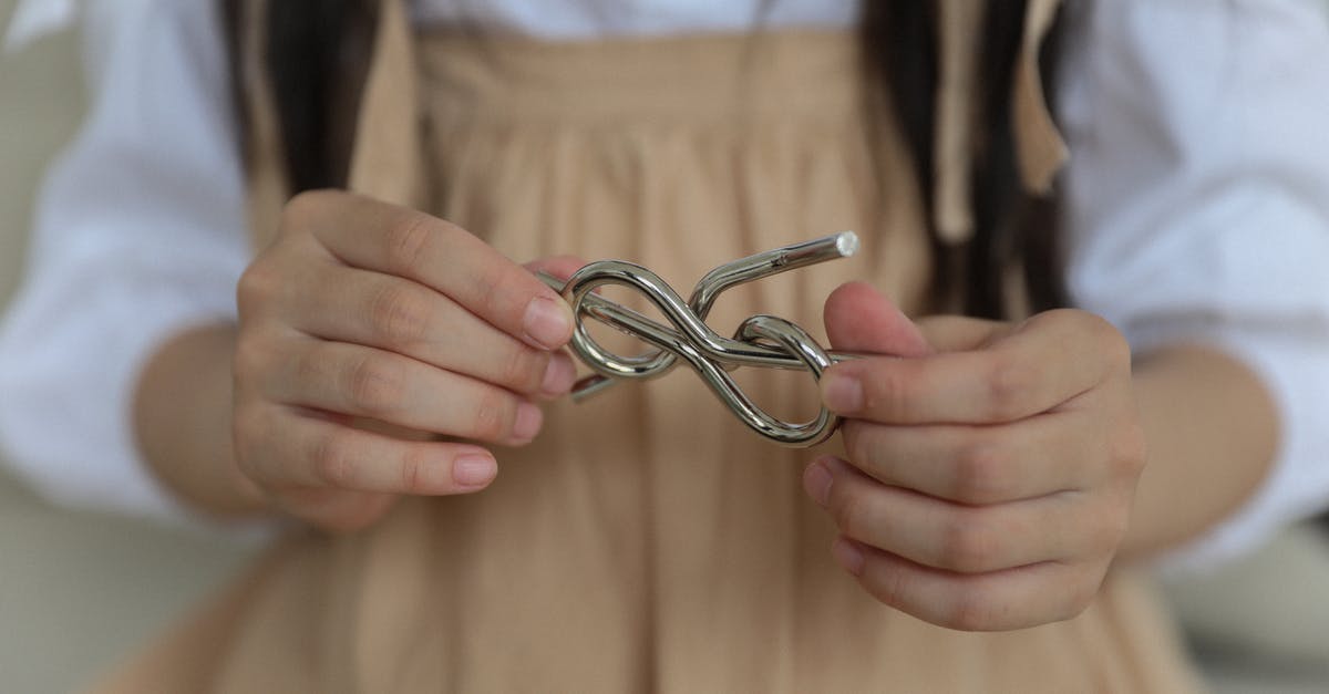 How to solve the language problem in Ankara, Turkey? - Crop anonymous child in casual wear holding metal wire brain teaser in shape of knot while playing at home