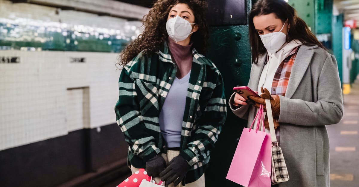 How to stay safe when using an autocaravan? - Female in protective mask using mobile phone while waiting for train on platform of subway station with friend standing with gift bags