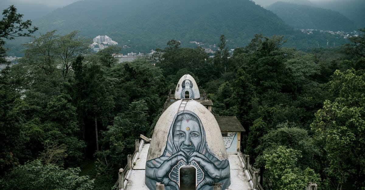 How to travel without transit visa from India to Stockholm? - From above small domed caves with graffiti on Buddhist meditation house rooftop located in Beatles Ashram in lush green rainforest against cloudy sky in India