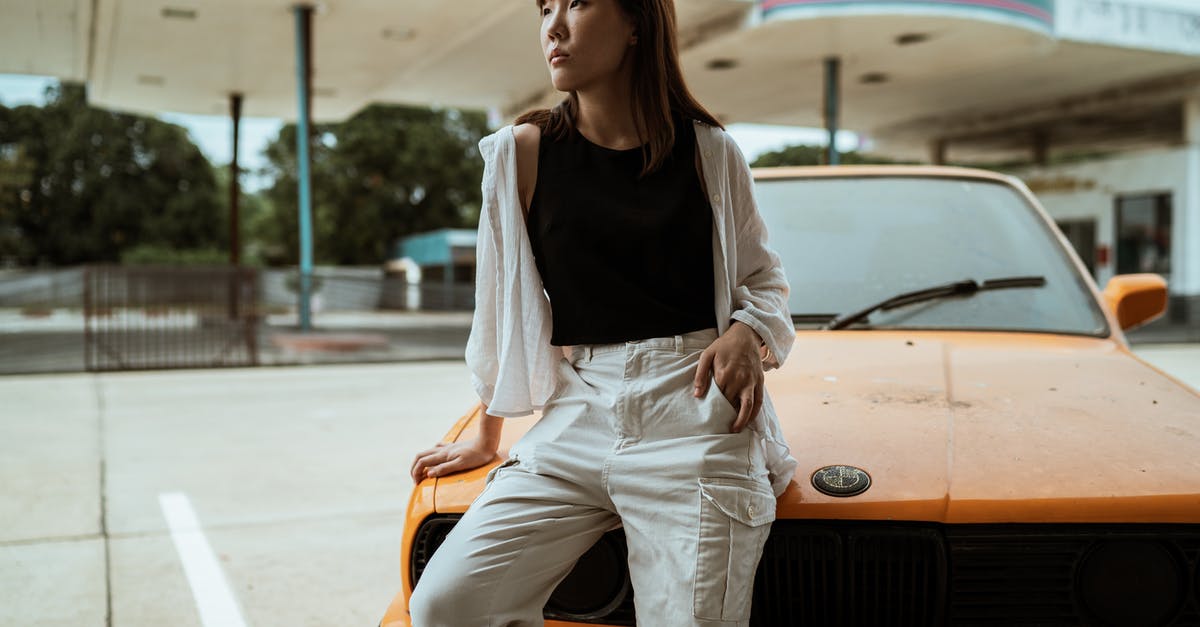 How to use a petrol/gas station in Greece? - Slim pensive Asian woman in casual wear sitting with hand in pocket on old timer automobile parked on asphalt road and looking away