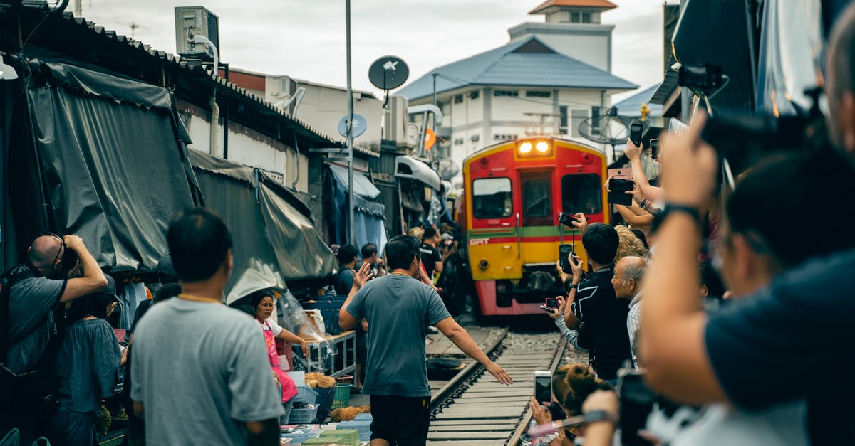 How to use cloud cover information to track auroras? - Back view of anonymous ethnic men and women standing near railway while taking photo on cellphones of old colorful tram on narrow street behind building under cloudy sky