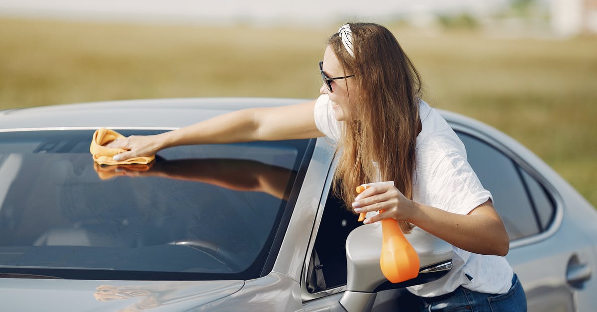 How to use hotmail / email for use on holiday abroad - Side view of cheerful female driver in sunglasses and casual clothes cleaning windshield of modern car with microfiber cloth and spray bottle against green field