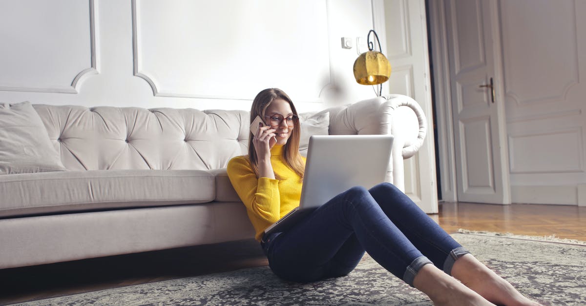 How to use payphone for calls within Cuba? - Smiling barefoot female in glasses and casual clothes using laptop and having phone call while sitting on floor leaning on sofa and working on laptop against luxury interior of light living room