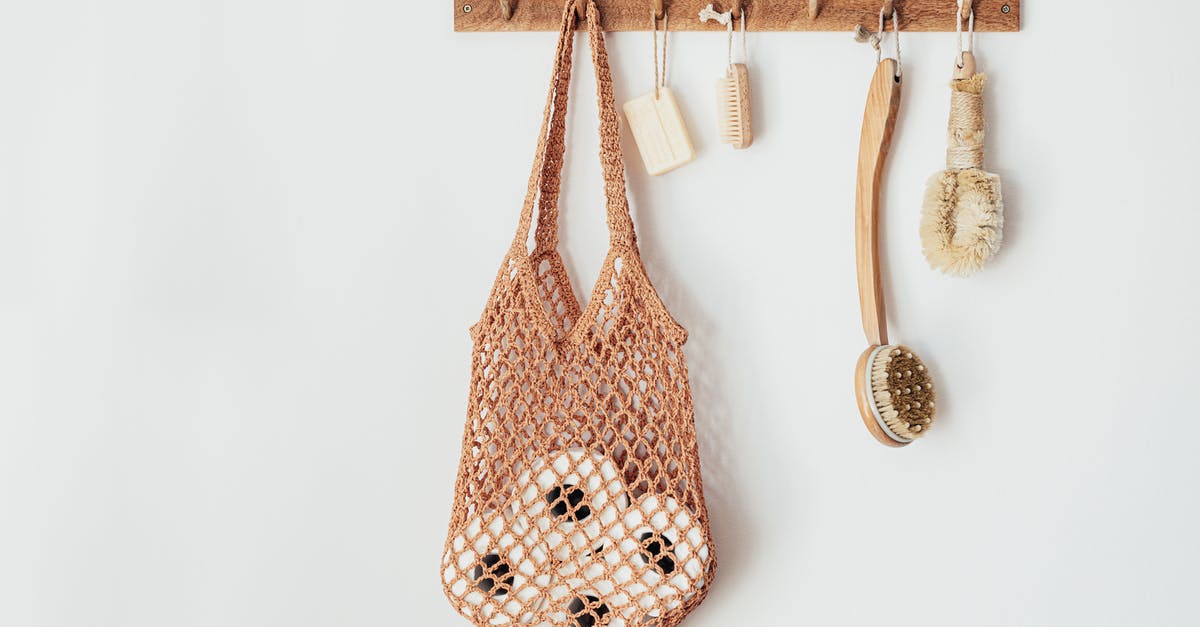 How to use toilet paper - Composition with assorted wooden body brushes of different sizes with organic soap and string bag filled with toilet paper rolls hanging on wooden hanger on white wall in bathroom