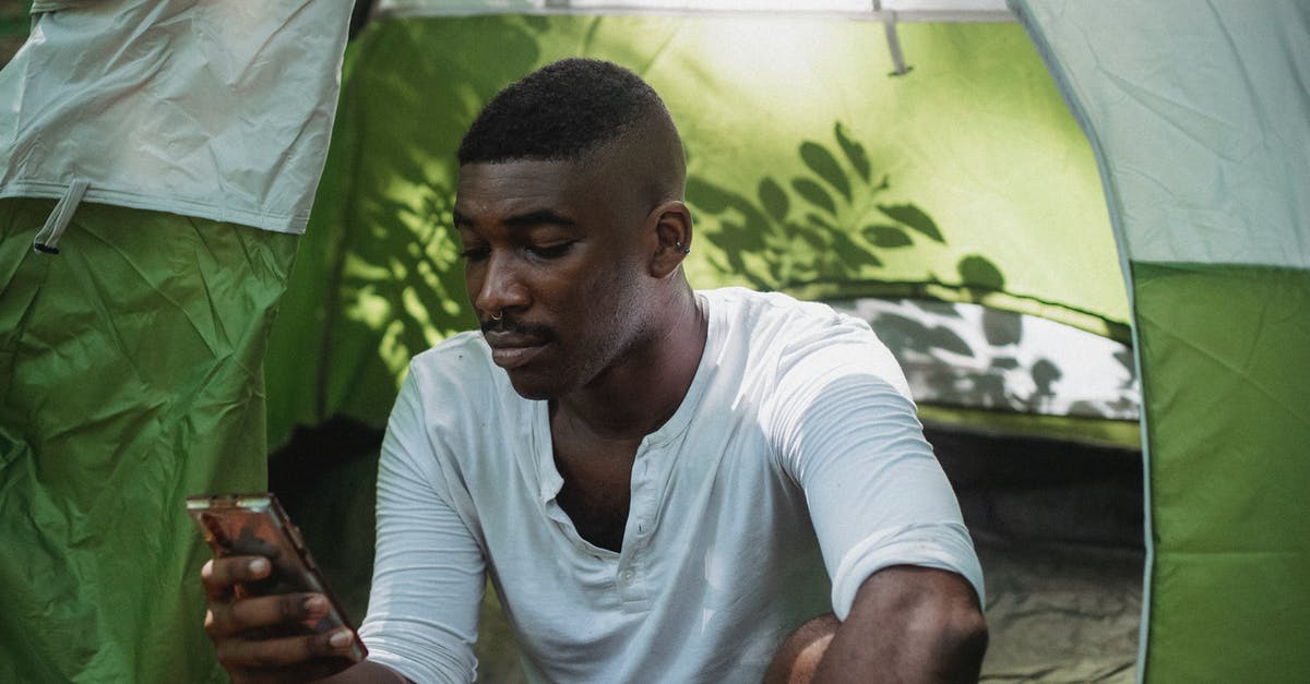 How to use trekking clothes? - Serious black man using smartphone in tent