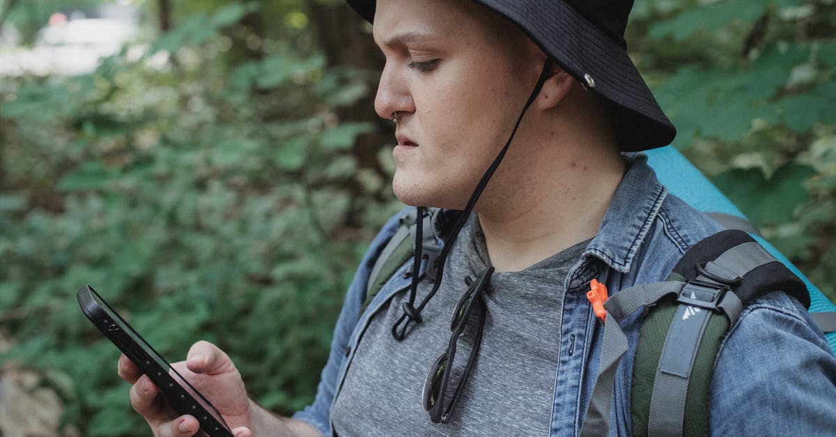 How to use trekking clothes? - Focused young male backpacker checking location on smartphone in nature