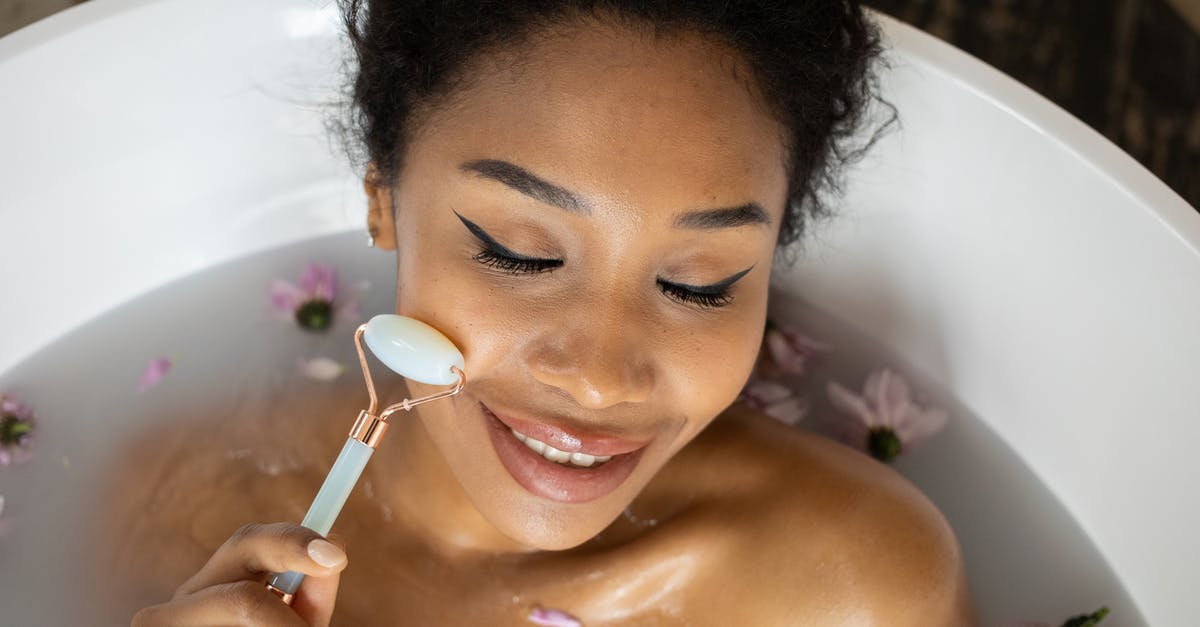 How ubiquitous are home water filtration systems in the USA? [closed] - From above of smiling ethnic female with closed eyes massaging face with jade roller while taking bath with flowers