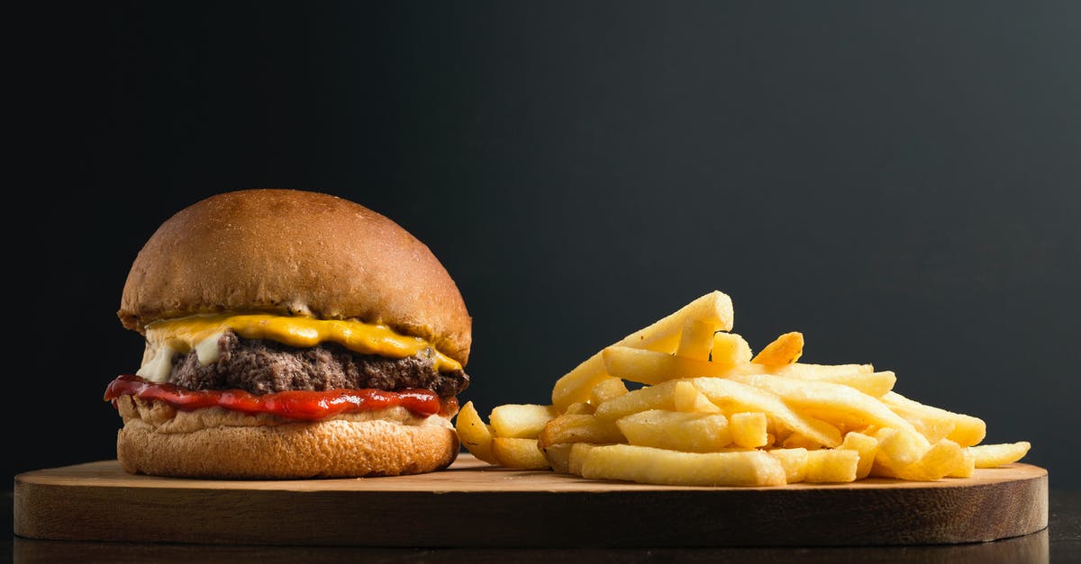 How useful/important is French in Montreal? - Appetizing burger with meat patty ketchup and cheese placed on wooden table with crispy french fries against black background