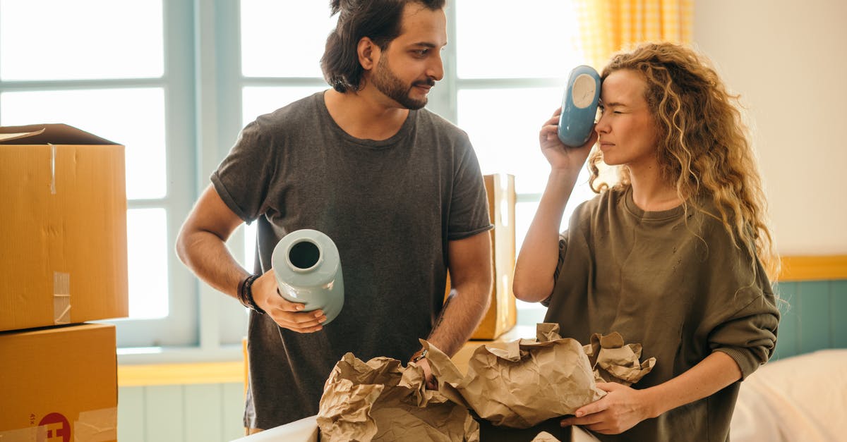 Husband and Wife TSA PRE-Check Changes - Satisfied adult bearded ethnic man and playful woman with curly hair wearing casual t shirts unboxing ceramics for home decoration from carton boxes while moving in new apartment