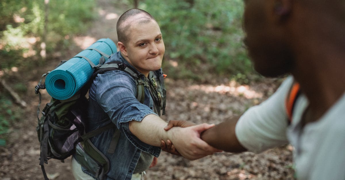 I need help regarding travel to Lisbon from Pakistan [duplicate] - Crop anonymous African American traveler helping friend with backpack with hiking equipment to climb up in forest