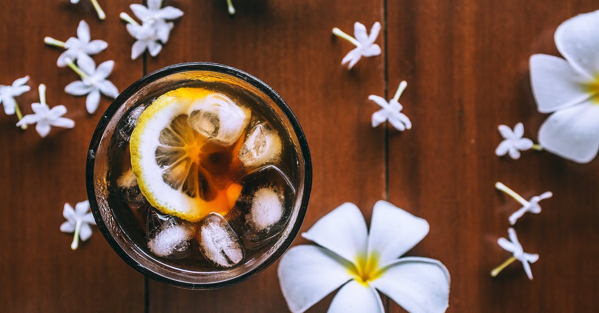 ICE from Frankfurt to Limburg - Top view of glass with fresh drink with slice of lemon and ice cubes on wooden background with plumeria flowers