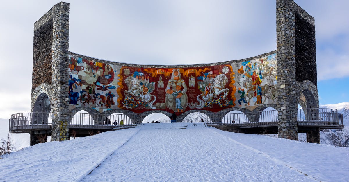 Identify location of old painting - Low angle of old stone arched Russia Georgia Friendship Monument with tile mural inside located on snowy hill in Gudauri