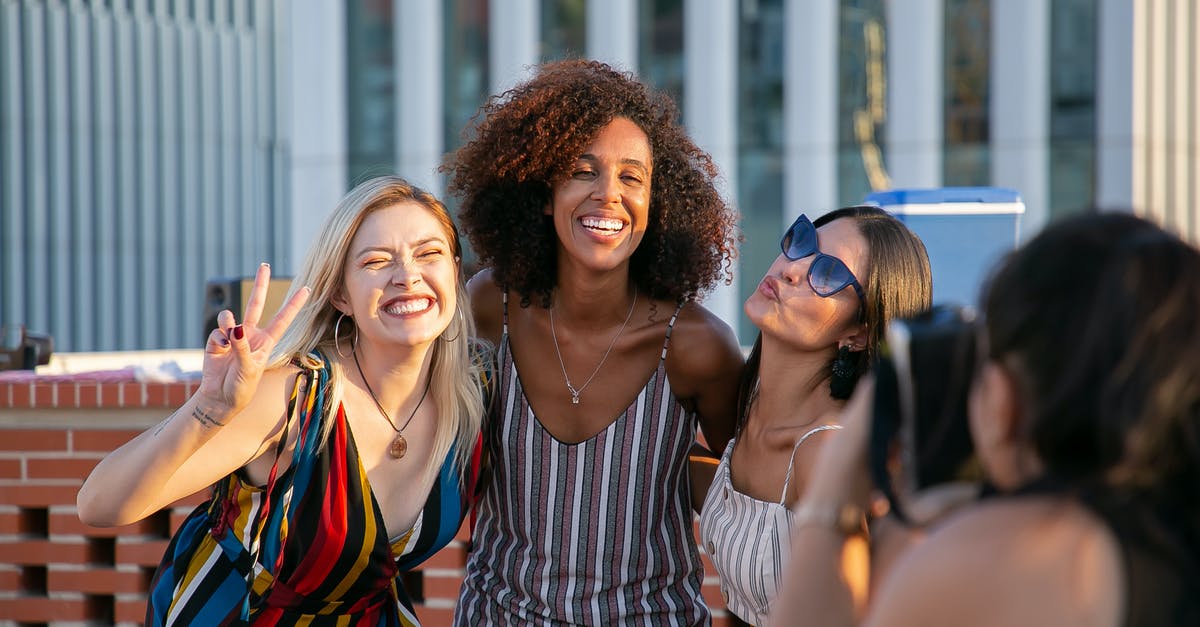 Identify the building in this picture - Unrecognizable female photographer taking picture of cheerful young multiracial female friends smiling and showing V sign during party on modern building rooftop