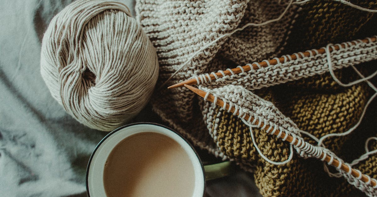 If arriving in Estonia in winter from a warm climate, is it easy to find good secondhand winter clothes? - From above of cup of hot coffee placed on bed with handmade knitted plaid with needles and wool yarn