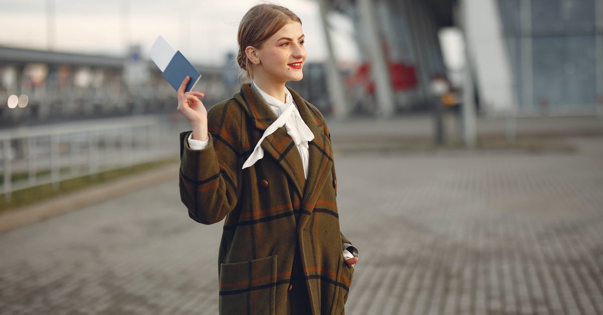 If my ticket allows me to take a maximum of 23 kg luggage, can I take two pieces with me whose total weight is less than 23 kg? - Cheerful female passenger wearing trendy plaid coat taking passport and ticket in raised hand while standing on pavement near modern building of airport outside and looking away with smile