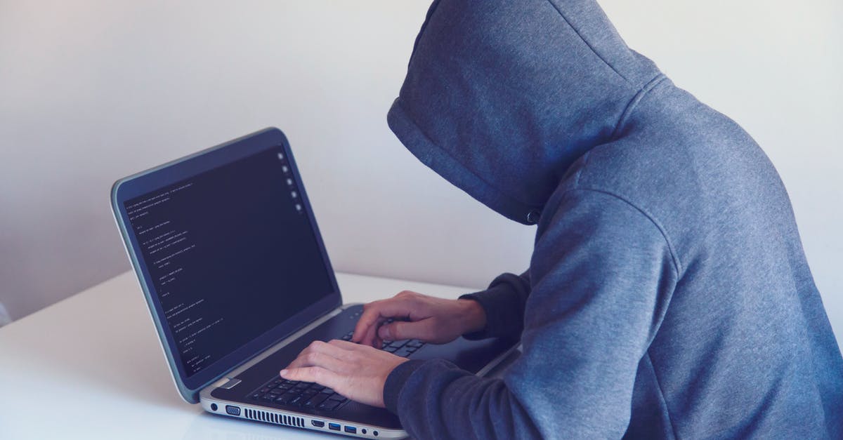 Immi account password recovery without answering security questions - Side view of unrecognizable hacker in hoodie sitting at white table and working remotely on netbook in light room near wall