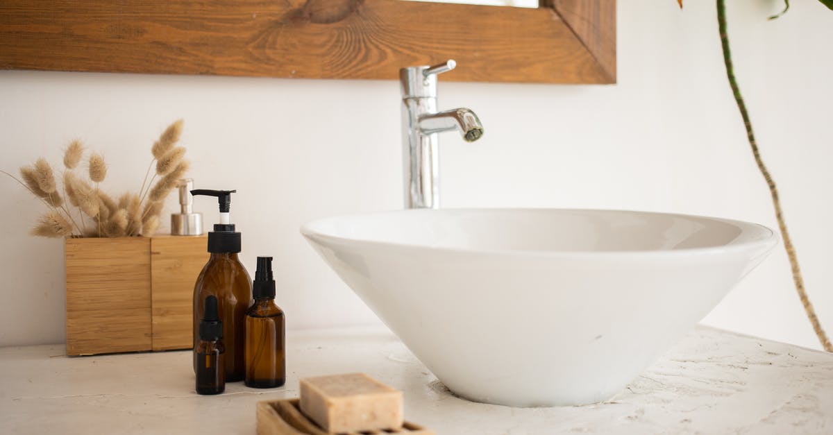 Importing wooden trinkets into New Zealand and Australia - Interior of bathroom table with soap and cosmetic oil placed near white sink and faucet under mirror in wooden frame in modern apartment