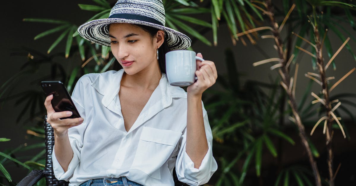 In Asian restaurants and airlines is it correct etiquette to use the hot towel on my face? - Young Asian lady wearing stylish outfit sitting in wicker armchair in greenery and browsing smartphone while drinking hot beverage