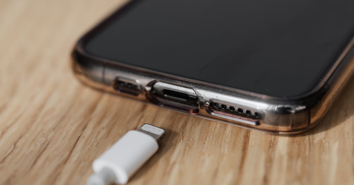 In Taiwan, what do you call those covered walkways? - Modern cellphone in transparent cover with closeup of charging input and mobile phone white charger cable usb connector on wooden table