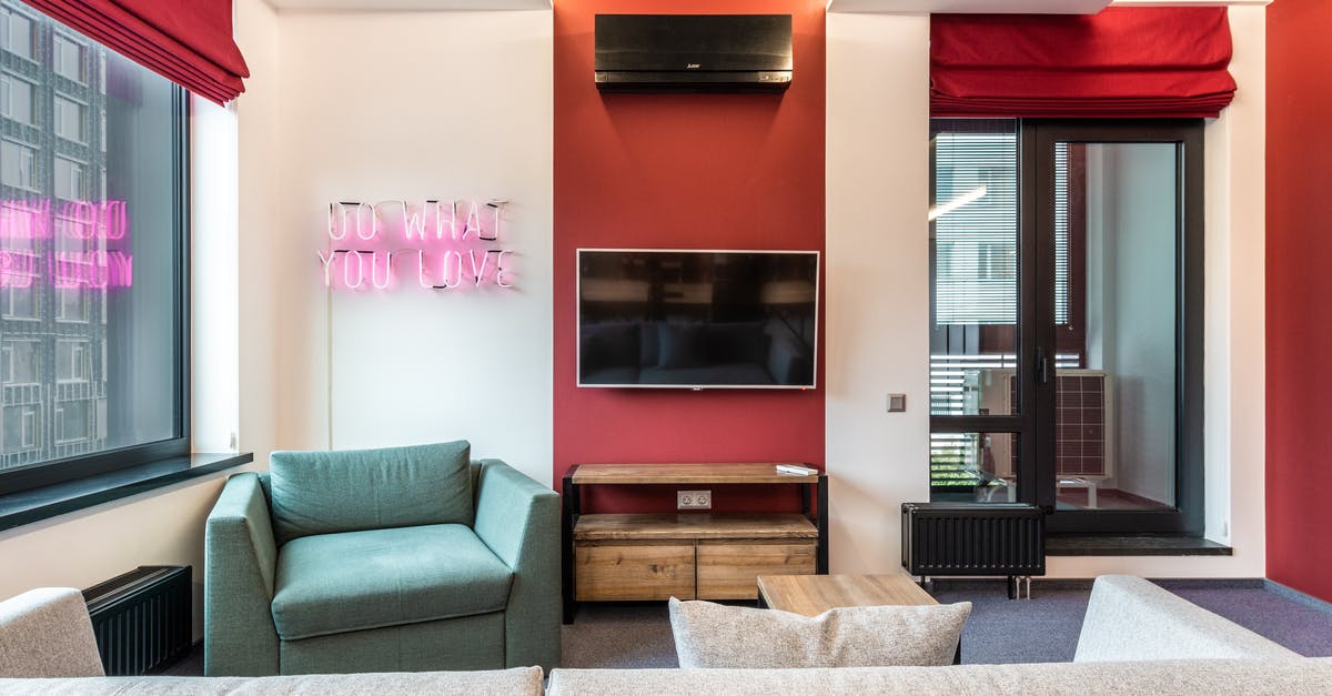 In the UK, what rights do you have if a hotel is overbooked? - Interior of modern office lounge zone with sofa and armchair with table near window next to TV on wall and neon signboard with text do what you love near door