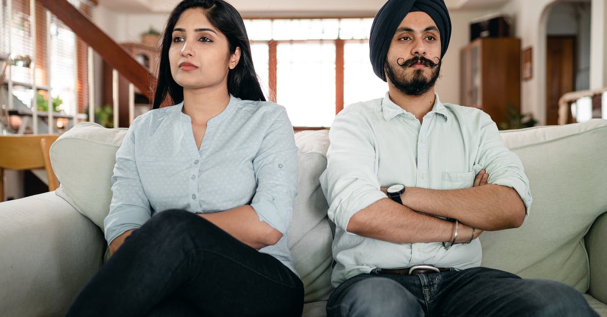 Indian B1 B2 visa crossing the border at San Diego - Resentful young Indian couple ignoring each other while sitting on couch together with crossed arms