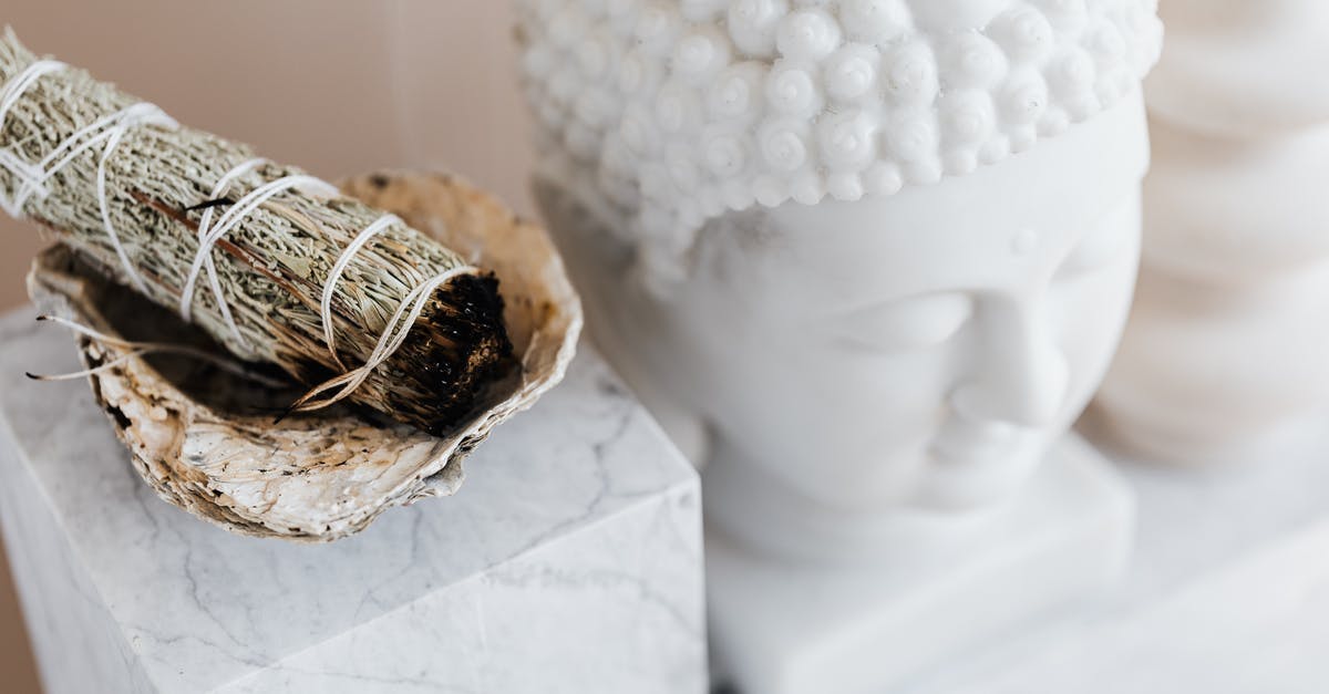 Indian Citizen applying for UK visa from UAE - From above of sage candle in bowl placed on white marble shelf near plaster Buddha bust and creative shape vase for home decoration