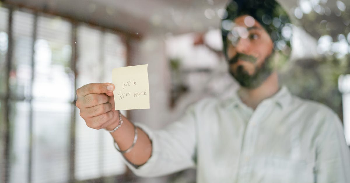 Indian National, Transit through Dublin - Indian guy in turban and shirt with curled mustache sticking paper with INDIA STAY HOME inscription while standing behind glass wall during COVID 19 pandemic