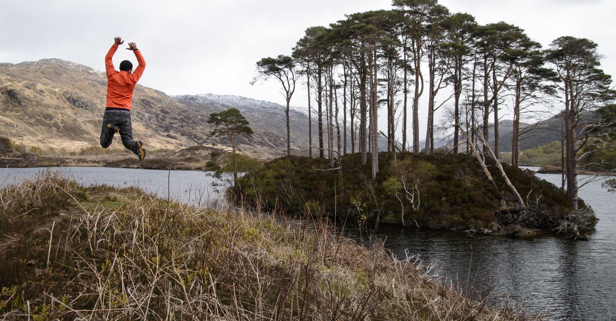 Indian passport traveling to Scotland - Man in Orange Long-sleeved Shirt Jumping on Lake Near Tall Trees at Daytime