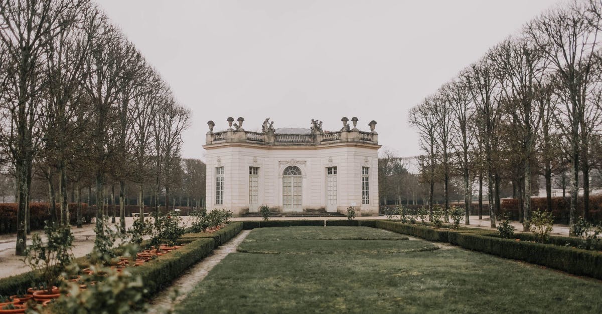 Indian traveling to Thailand with residence in Europe - Exterior of ornamental modern palace with white walls and big cozy windows decorated with statues on roof located in beautiful park on autumn overcast day