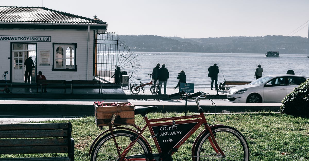 Information about public transport in Greece - Bicycle with pointer on black board parked on crowded paved embankment with car and building against calm sea and mountain on background