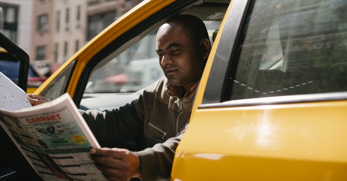 Information about public transport in Greece - Concentrated male driver in casual clothes sitting in taxi during break and reading newspaper