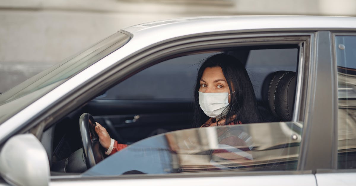 Insurance claim for cancelled trip due to sickness - Young woman wearing medical mask driving car