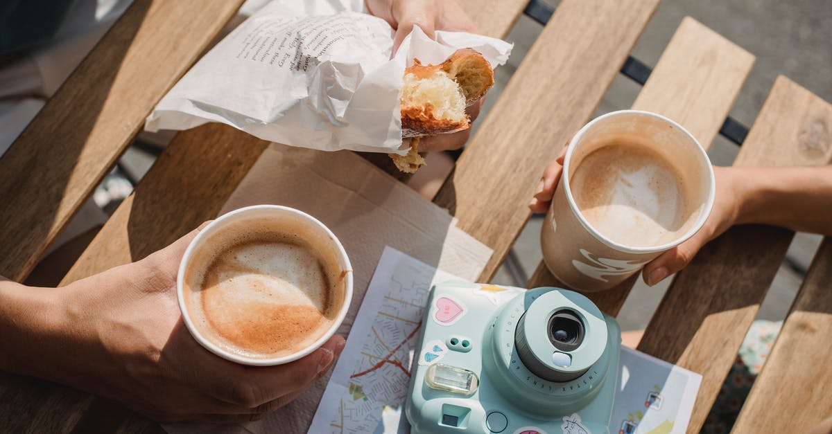 Interactive map for when and where to go - From above of crop anonymous couple with disposable glasses of cappuccino and photo camera on table in street cafeteria