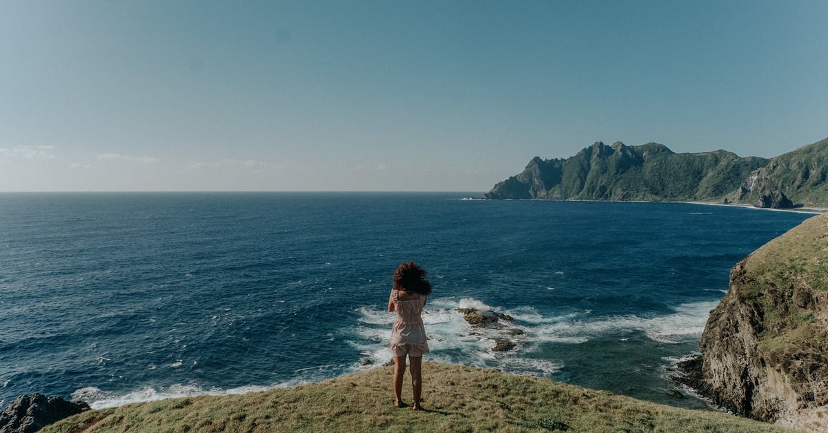 Intercity Travel in the Philippines - Back View Photo of Woman in White Top and Shorts Standing on Cliff Near Body of Water