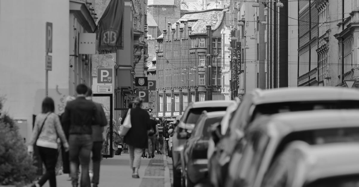 Inter-country one-way car rental in Europe? - Black and white unrecognizable passers by strolling on paved sidewalk along narrow road in old city district