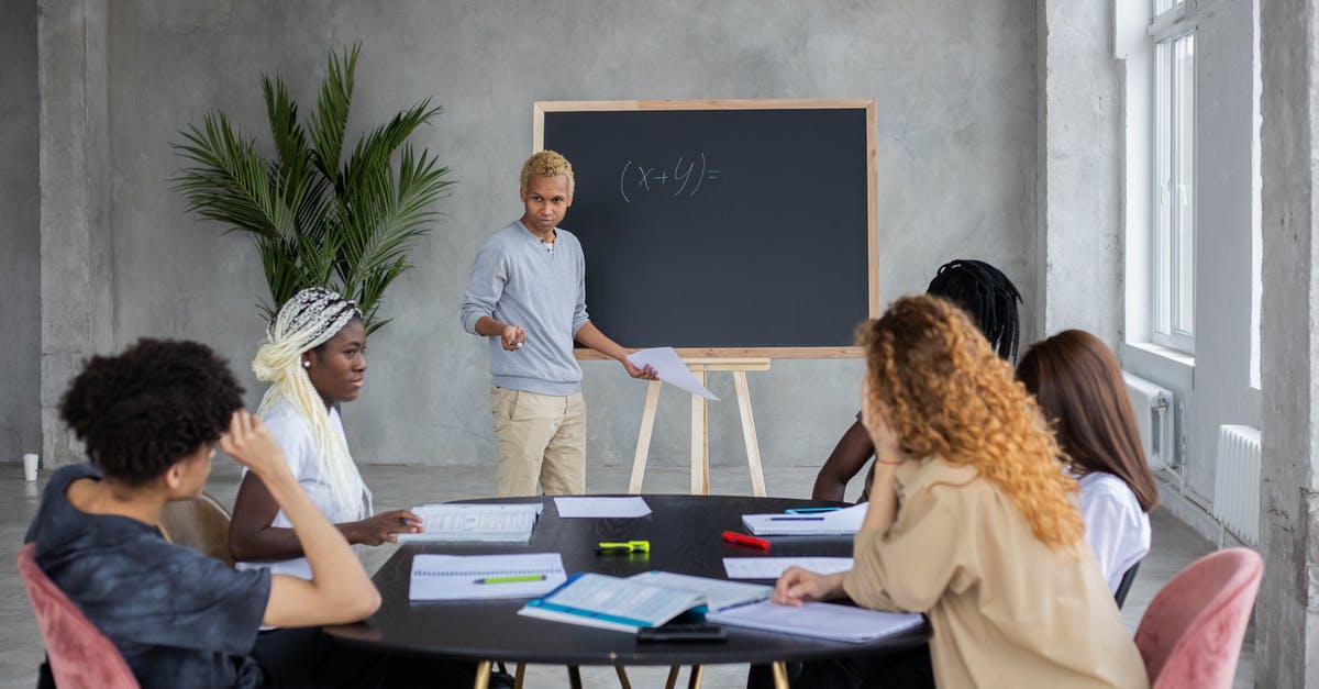 International Student With a UK Visa Question - African American student explaining mathematic equation to diverse classmates while doing homework together in spacious room