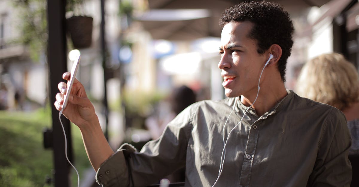 Internet access using mobile phone in Argentina - Side view of black male wearing summer shirt using smartphone for video chatting and sitting on outdoor terrace while communicating on social media