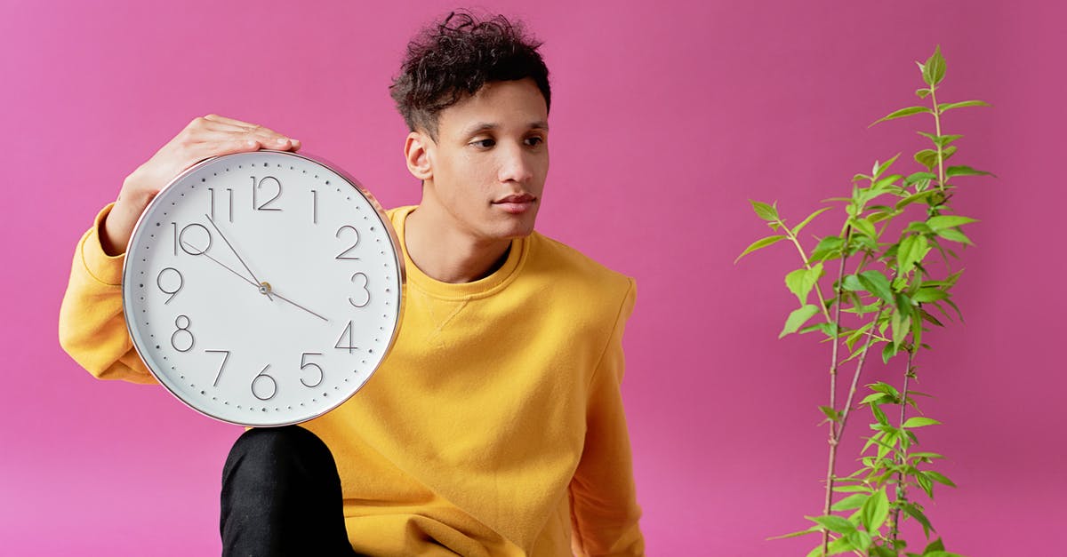 Is 1 hour and 15 minutes enough for transit in Amsterdam airport? - A Man in Yellow Sweater Sitting Near the Plant while Holding a Clock
