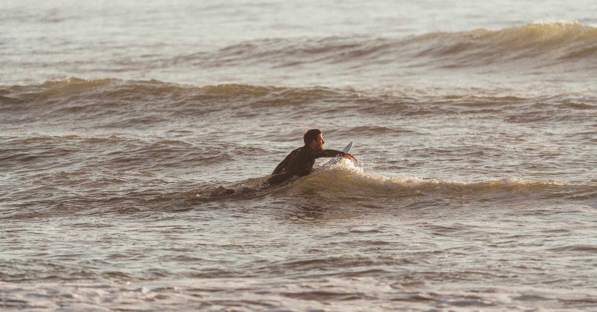 Is 2 hours enough at AMS to catch at train? - Side view of sporty male with surfboard catching wave in rippling water of ocean