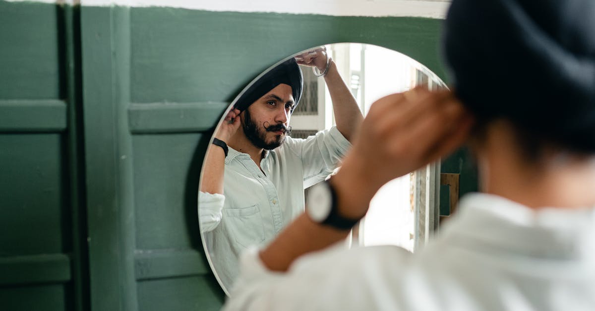 Is it considered uncouth to check in early into a hotel? - Back view of Indian man with beard wearing turban and looking in mirror while standing in front of mirror in modern bathroom