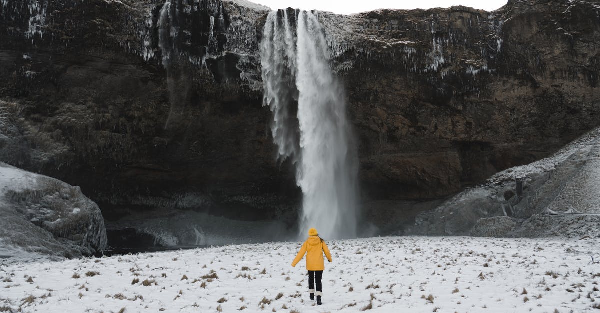 Is it legal to travel with a 1W/1000mW laser? - Person in Red Jacket Standing on White Snow Covered Ground Near Waterfalls