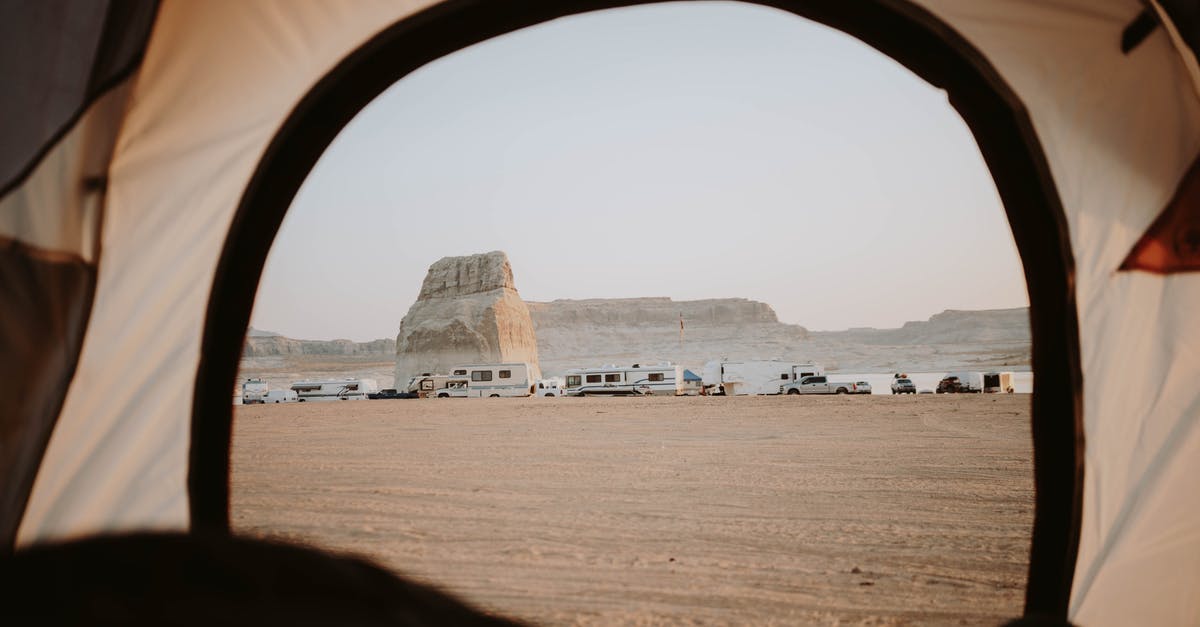 Is it legal to wild camp (with a car) in Ireland? - View of sandy beach with distanced cars parked on seaside with rocky cliffs through opened tent in nature with cloudless sky