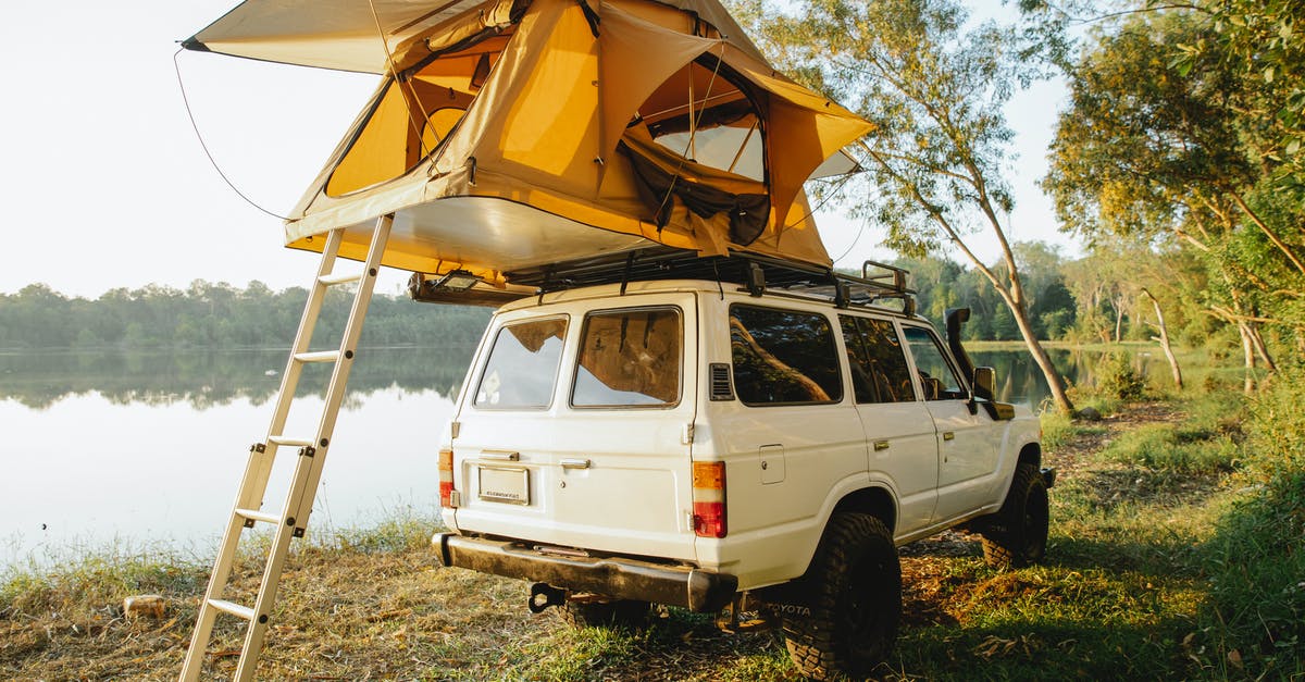 Is it legal to wild camp (with a car) in Ireland? - Off road car with camping tent on roof parked on grassy coast of picturesque lake surrounded by lush green trees against cloudless blue sky