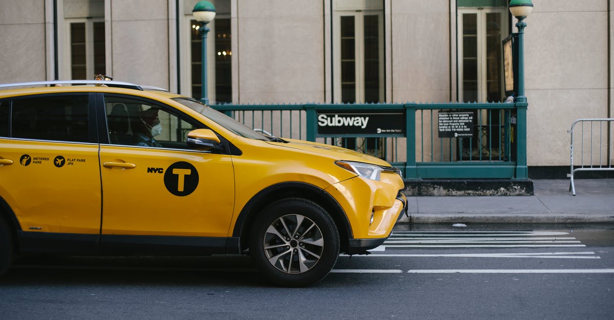 Is it normal/expected to tip taxi drivers in the UK? - Contemporary yellow taxi with driver in medical mask standing on empty road near modern building and subway station entrance during coronavirus pandemic in New York USA