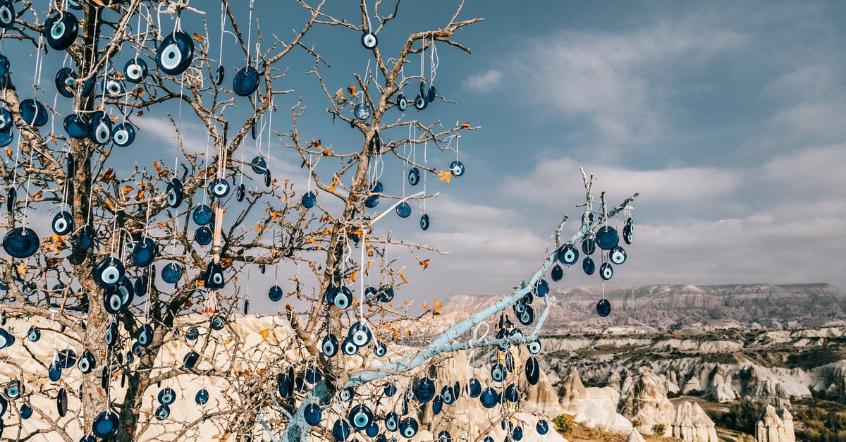 Is it okay to carry a small titanium souvenir in baggage - Amulets of blue glass reminding eye hanging on tree branches over are with volcanic formations