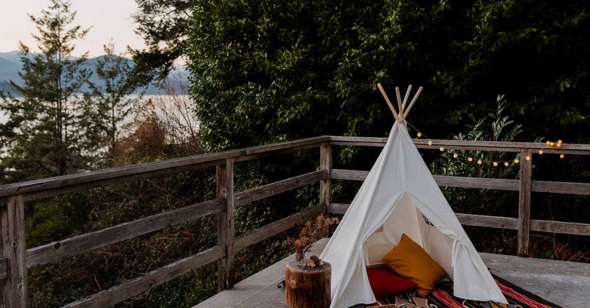 Is it possible to camp in a tent in Finland - Boho styled tent with rug and pillows located on terrace with wooden fence with picturesque view to sea forest and mountains